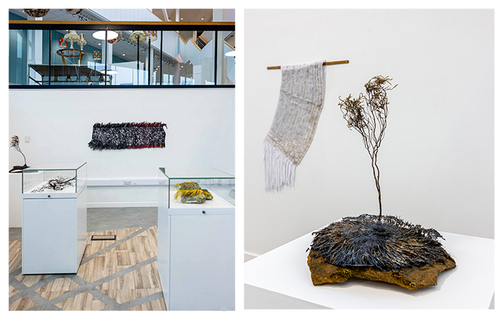 An exhibition of work, with two glass vitrines with artefacts in the front and a tapestry made of melted shoelaces on the wall behind