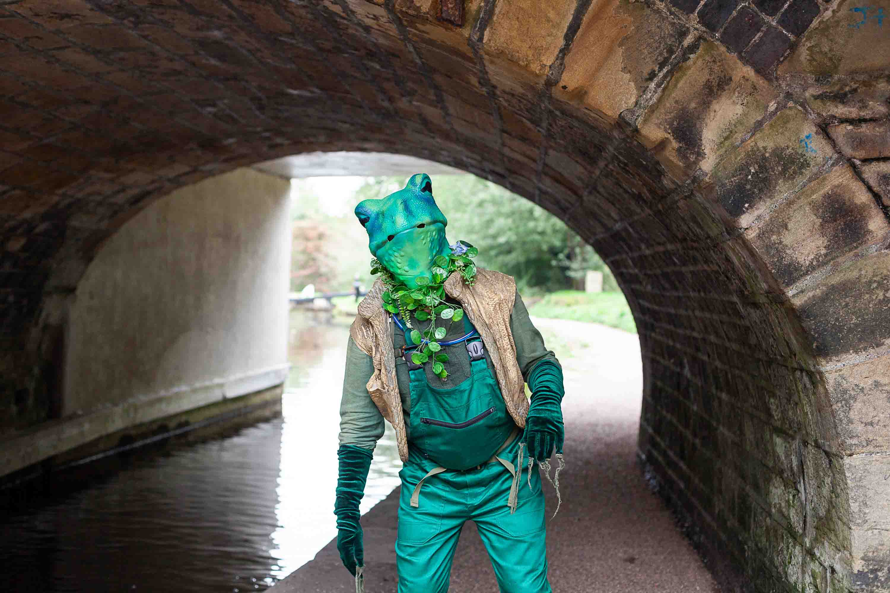 A man dressed as as frog next to a canal under an arch.