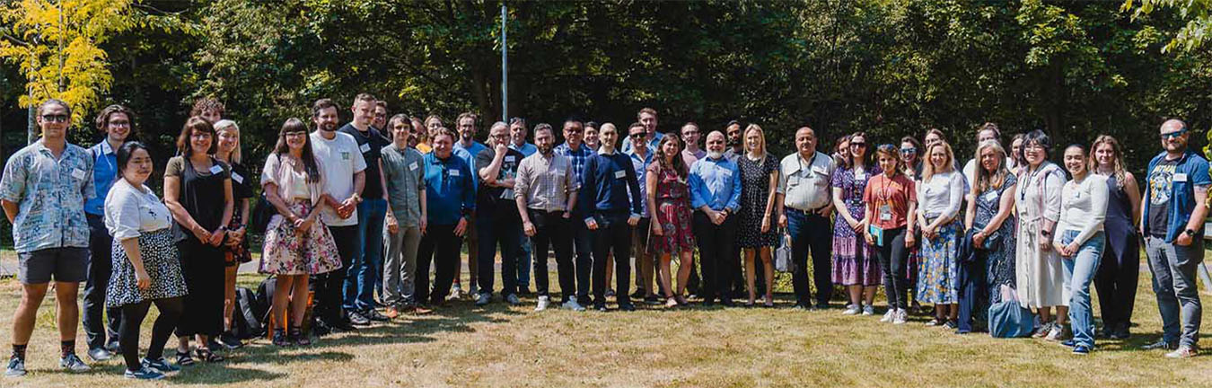 a group of about 40 people standing outside, smiling in the sun