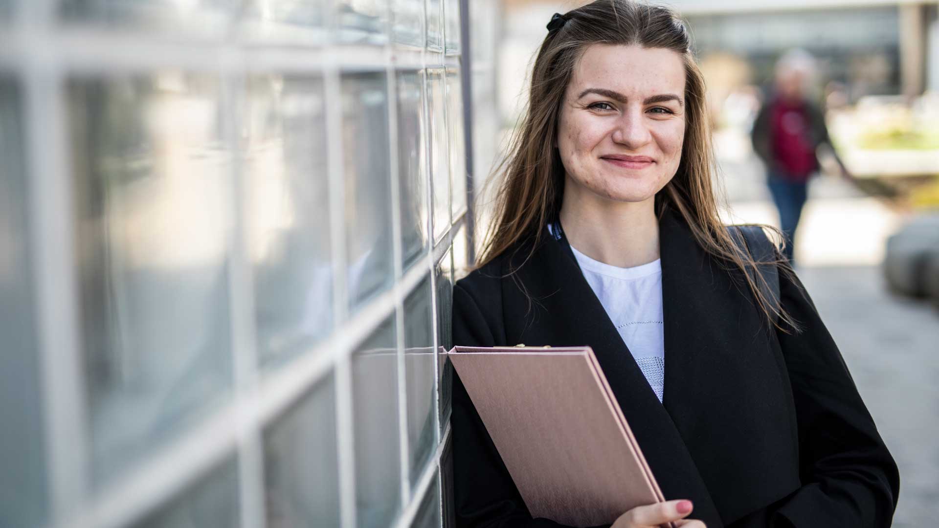student holding notepad and leaning on wall