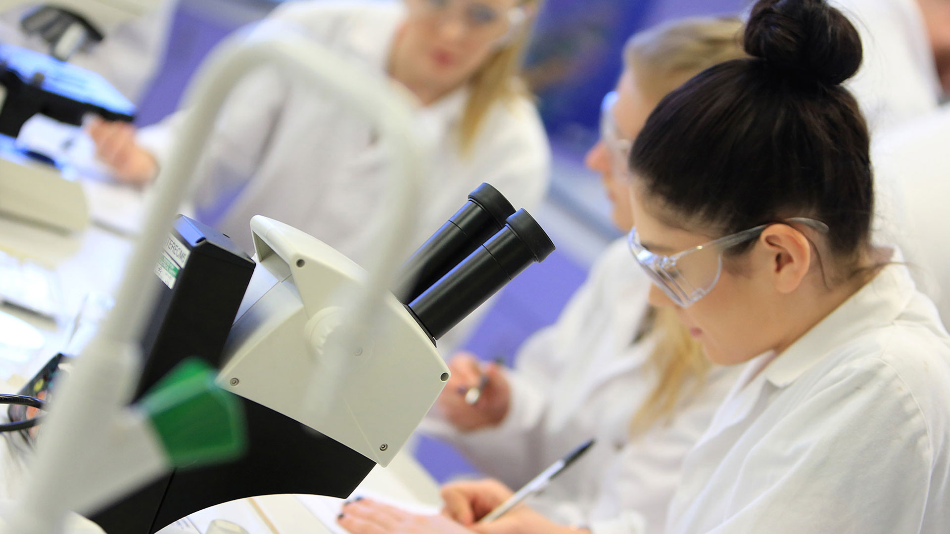 Female researcher in a lab recording data from a microscope