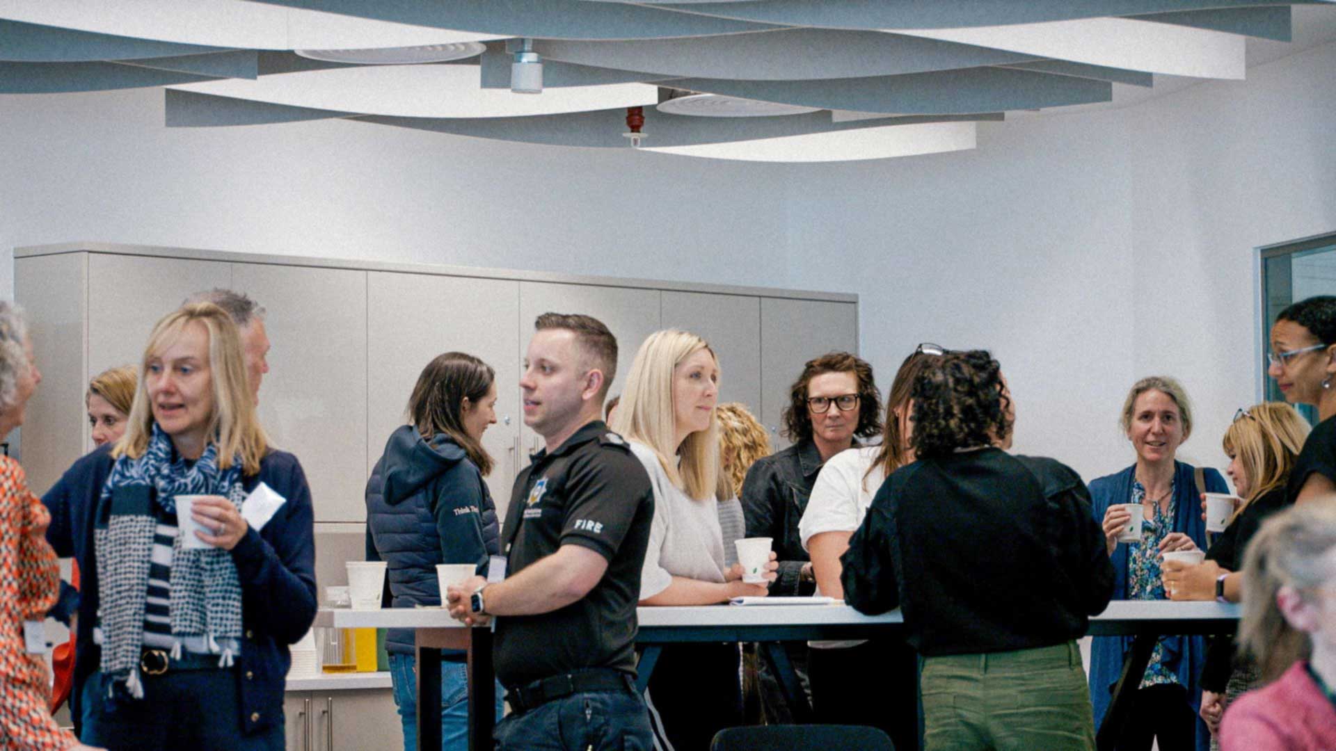 People standing around tall tables, with drinks and chatting with smiles.